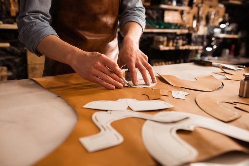 Close up of a shoemaker measuring and cutting leather in a workshop